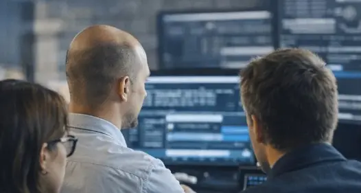 Profissionais de tecnologia analisando dados e sistemas em telas de computador em ambiente corporativo, representando monitoramento, TI e tomada de decisão estratégica para produzir um vídeo.