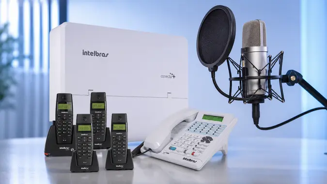 Central PABX com telefones empresariais e microfone profissional, representando gravação de mensagens para URA e espera telefônica.